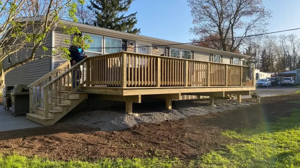 Wide pressure treated wood deck with picket railing and side stairs along the back of a gray sided modular home, by NG Masonry serving Henrietta NY