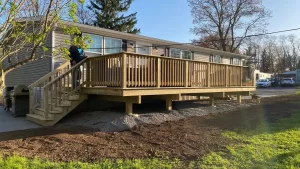 Wide pressure treated wood deck with picket railing and side stairs along the back of a gray sided modular home, by NG Masonry serving Henrietta NY