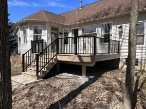 Tan composite deck with black aluminum railing and stairs at the back of a white sided ranch home, by NG Masonry serving Rochester NY