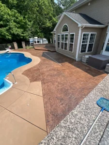 Recolored and resealed copper toned stamped concrete pool deck wrapping a kidney shaped in ground pool at a tan sided home, by NG Masonry serving Chili NY