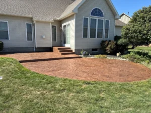 Recolored and resealed warm terra cotta toned ashlar slate stamped concrete patio with matching step risers at a tan sided home with arched windows, by NG Masonry serving Webster NY