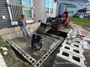 NG Masonry crew finishing fresh concrete inside a block foundation form for a home addition with a tracked machine moving block on site, serving Brighton NY