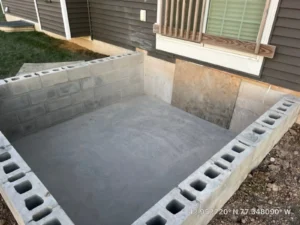 Newly laid concrete block foundation walls for a home addition next to a gray sided home with a freshly poured concrete slab inside, by NG Masonry serving Brockport NY