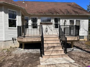 Light tan composite deck with black aluminum railing and center stairs at the back of a white sided ranch home, by NG Masonry serving Brighton NY