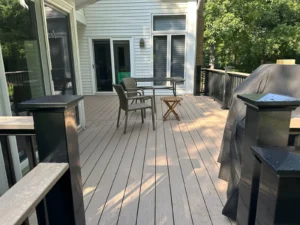 Light gray composite deck boards viewed from sliding glass doors of a white sided home with patio furniture and a covered grill, by NG Masonry serving Brockport NY