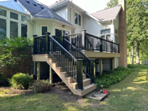 Elevated tan composite deck with black aluminum railing and stairs at a luxury home with sunroom and stone chimney, by NG Masonry serving Canandaigua NY