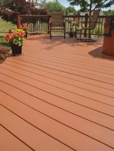 Closeup of redwood toned composite deck boards with bronze railing, patio chairs, and a flower planter beside a hot tub, by NG Masonry serving East Rochester NY