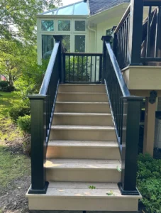 Tan composite deck stairs with black aluminum railing leading up to a deck beside a luxury home sunroom, by NG Masonry serving Farmington NY