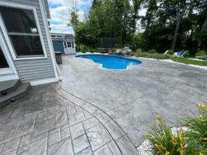 Wide gray ashlar slate stamped concrete pool deck wrapping a kidney shaped pool in a backyard, by NG Masonry serving Brockport NY