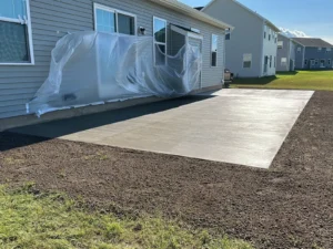 Plain rectangular broom finish concrete patio freshly poured beside a tan sided home, by NG Masonry serving Canandaigua NY