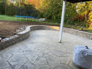 Random flagstone pattern stamped concrete patio with stone retaining seat wall in a backyard, by NG Masonry serving Canandaigua NY