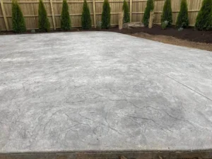 Gray broom finish concrete patio enclosed by a wood plank privacy fence, by NG Masonry serving Chili NY
