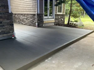 Dark gray broom finish concrete patio with stamped border at a stone veneer entry, freshly poured by NG Masonry serving East Rochester NY