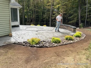NG Masonry worker pressure washing a freshly stamped concrete patio with stone seat wall, serving Farmington NY