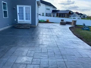 Wide stamped concrete patio with steps in front of a red sided home with second story deck, by NG Masonry serving Gates NY