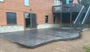 Gray slate textured stamped concrete patio with rock faced edge behind a red sided home, by NG Masonry serving Geneva NY