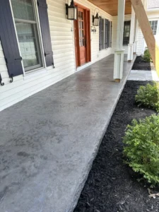 Long charcoal slate textured stamped concrete porch slab beside a white sided home with dark shutters, by NG Masonry serving Greece NY