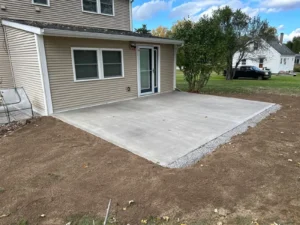Plain rectangular broom finish concrete patio behind a tan two story home, freshly poured by NG Masonry serving Henrietta NY