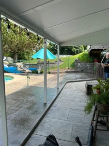 Charcoal slate textured stamped concrete patio under a covered porch with string lights overlooking a pool, by NG Masonry serving Hilton NY