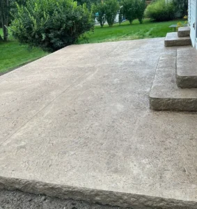 Sandstone tan stamped concrete patio with rock faced edge and stone steps at a white sided home, by NG Masonry serving Marion NY
