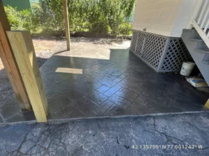 Charcoal slate textured stamped concrete patio in herringbone pattern under a covered deck, by NG Masonry serving Mendon NY