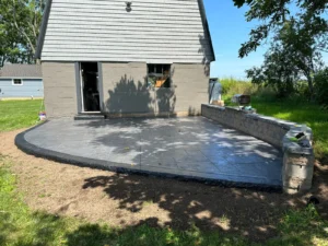 Curved charcoal slate textured stamped concrete patio with stone retaining wall at a gray block home, by NG Masonry serving Newark NY