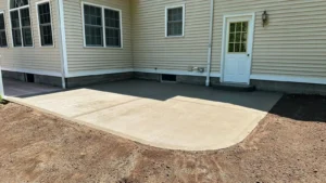 Square broom finish concrete patio behind a cream sided home with white side door, by NG Masonry serving Penfield NY
