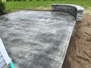 Modern gray wood plank stamped concrete patio with fire table and Adirondack seating at a gray sided two story home, by NG Masonry serving Webster NY