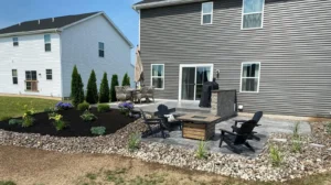 Charcoal slate textured stamped concrete patio in a herringbone pattern between siding and a privacy fence, by NG Masonry serving Williamson NY