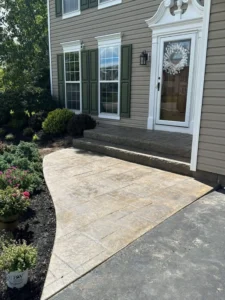 Tan ashlar slate stamped concrete walkway with matching front step leading to the entry of a tan sided home with green shutters, by NG Masonry serving Batavia NY
