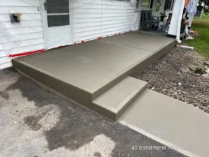 Wide tan broom finished concrete porch slab with step riser at a white sided home, freshly poured by NG Masonry serving Batavia NY