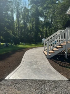 Curving gray slate stamped concrete walkway leading from a graveled path to a white wood deck staircase beside a pool, by NG Masonry serving Brighton NY