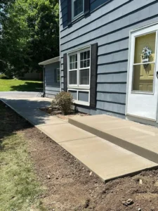 Light gray broom finished concrete walkway with matching front step at the entry of a gray shake sided home, by NG Masonry serving Brockport NY