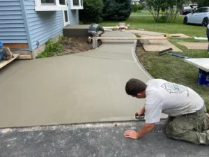 NG Masonry crew finishing a freshly poured wide curved concrete walkway with hand troweling alongside a blue sided home, serving Gates NY