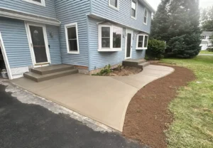 Wide curving tan broom finished concrete sidewalk wrapping along a blue sided two story home with two front entry steps, by NG Masonry serving Irondequoit NY