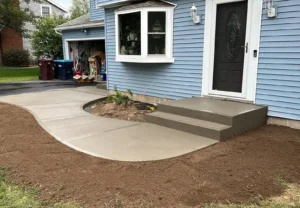 Curving light gray broom finished concrete walkway with matching front step risers leading from the driveway to the front door of a blue sided home, by NG Masonry serving Marion NY