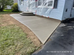 Light gray broom finished concrete walkway with round step landings at the side entry of a blue sided home, by NG Masonry serving Pittsford NY