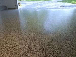 Closeup of a finished brown and tan flake epoxy garage floor coating extending out the open garage door to a stone landing, by NG Masonry serving Brighton NY