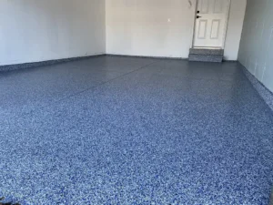 Empty garage with a finished blue and gray flake epoxy floor coating with side entry door visible, by NG Masonry serving Brockport NY