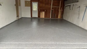 Wide finished gray flake epoxy floor coating inside a garage with wood paneled back wall and tools hanging on the right, by NG Masonry serving Fairport NY
