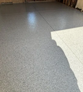 Closeup of a finished gray flake epoxy garage floor showing the chip blend texture and matching color step transition, by NG Masonry serving Farmington NY