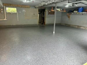 Empty basement with finished gray flake epoxy floor coating, support post in the center, and HVAC ducting along the ceiling, by NG Masonry serving Gates NY