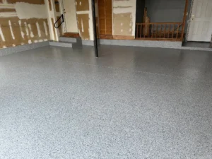Finished gray flake epoxy garage floor coating with curb riser and matching cove base trim against unfinished drywall walls, by NG Masonry serving Henrietta NY