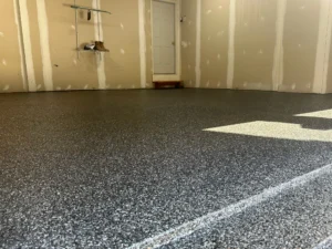 Low angle view of a finished black and white flake epoxy garage floor coating with a side entry door and tan painted walls, by NG Masonry serving Hilton NY