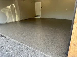 Empty two car garage with finished tan flake epoxy floor coating leading to a steel side entry door, tan painted walls, by NG Masonry serving Marion NY