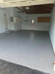 Two car garage with finished gray flake epoxy floor coating, exposed truss ceiling, side entry door, and wall mounted cabinets and storage, by NG Masonry serving Newark NY