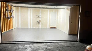 Empty two car garage at night with finished gray flake epoxy floor coating and a bicycle hanging on the left wall, by NG Masonry serving Penfield NY