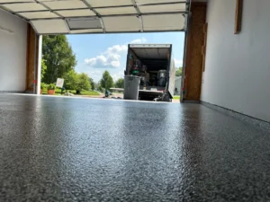 Low angle view of a glossy finished black flake epoxy garage floor looking out the open garage door to a moving truck in the driveway, by NG Masonry serving Pittsford NY