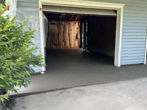 Open garage doorway with exposed wall insulation inside and a freshly poured smooth gray concrete floor extending to a gravel driveway, by NG Masonry serving Batavia NY