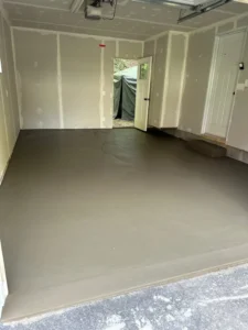Empty drywalled two car garage with a freshly poured smooth gray concrete floor and side entry door open to the yard, by NG Masonry serving Brockport NY